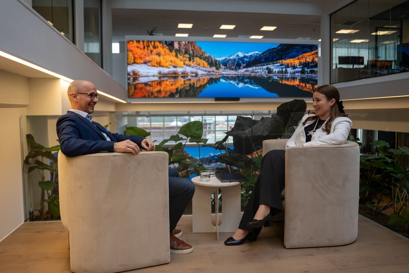 Two employees sit in communal area with large LED video wall 