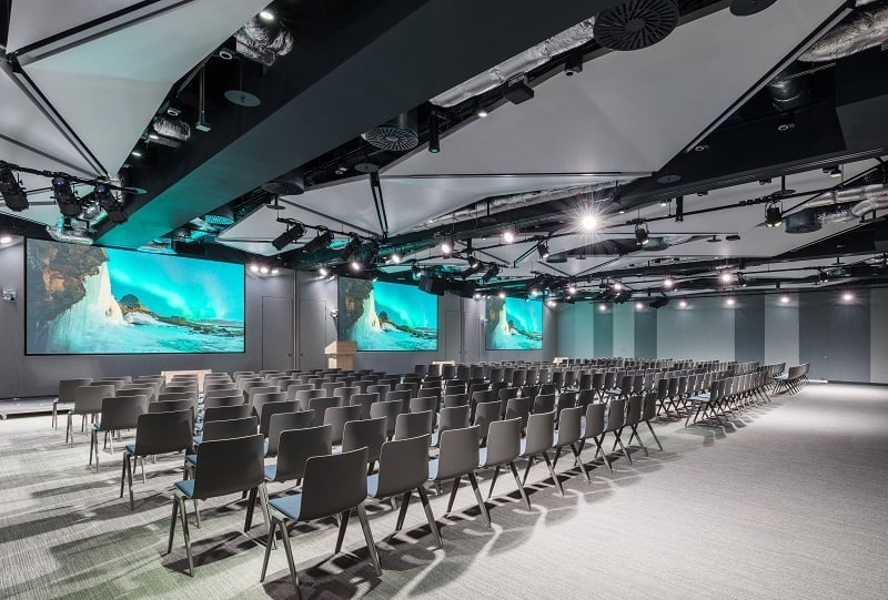 Large flexible conference venue with auditorium seating, multiple presentation screens and professional audiovisual technology